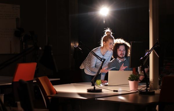 Two people working on a computer in a dimly lit room with a spotlight on them.