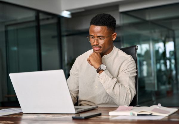 Man pondering while looking at his laptop in an office